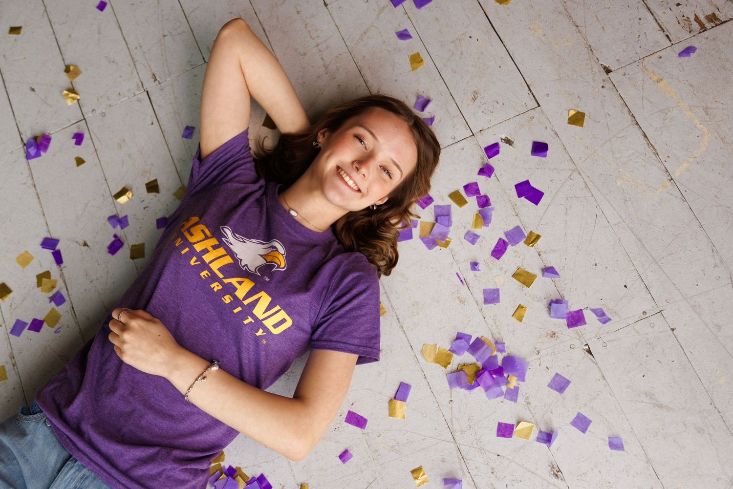 A high school senior girl laying on wooden floor with confetti.
