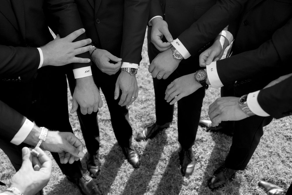 Hands of wedding guests clink champagne glasses together in a celebratory toast at an outdoor reception.