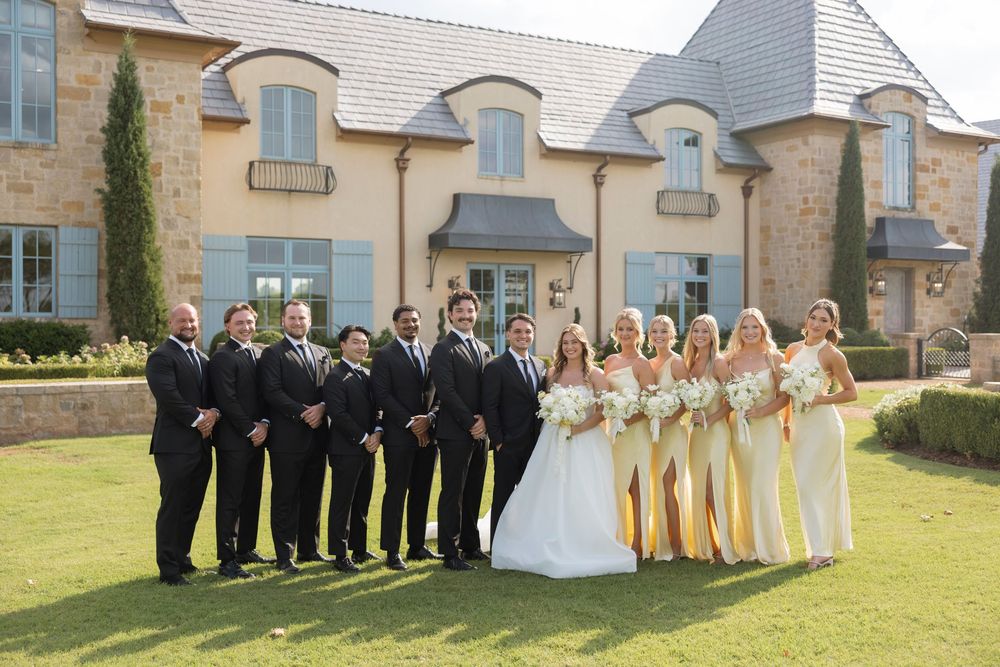 Wedding party poses in different group formations on a sunny lawn outside a stone building.