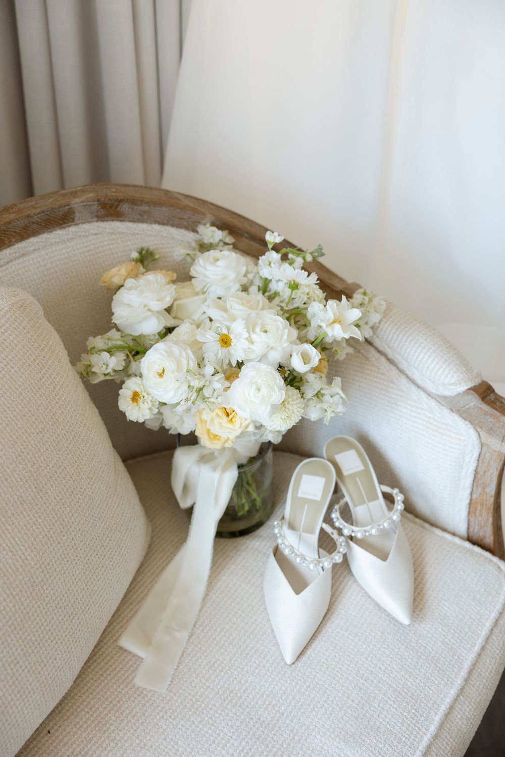 White bridal shoes and floral arrangement displayed on a textured beige surface.