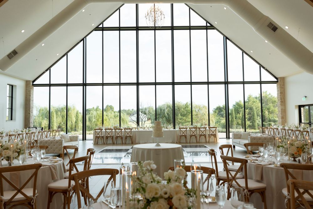 Elegant wedding reception venue with vaulted ceiling, white decor, and large arched windows overlooking scenic views.