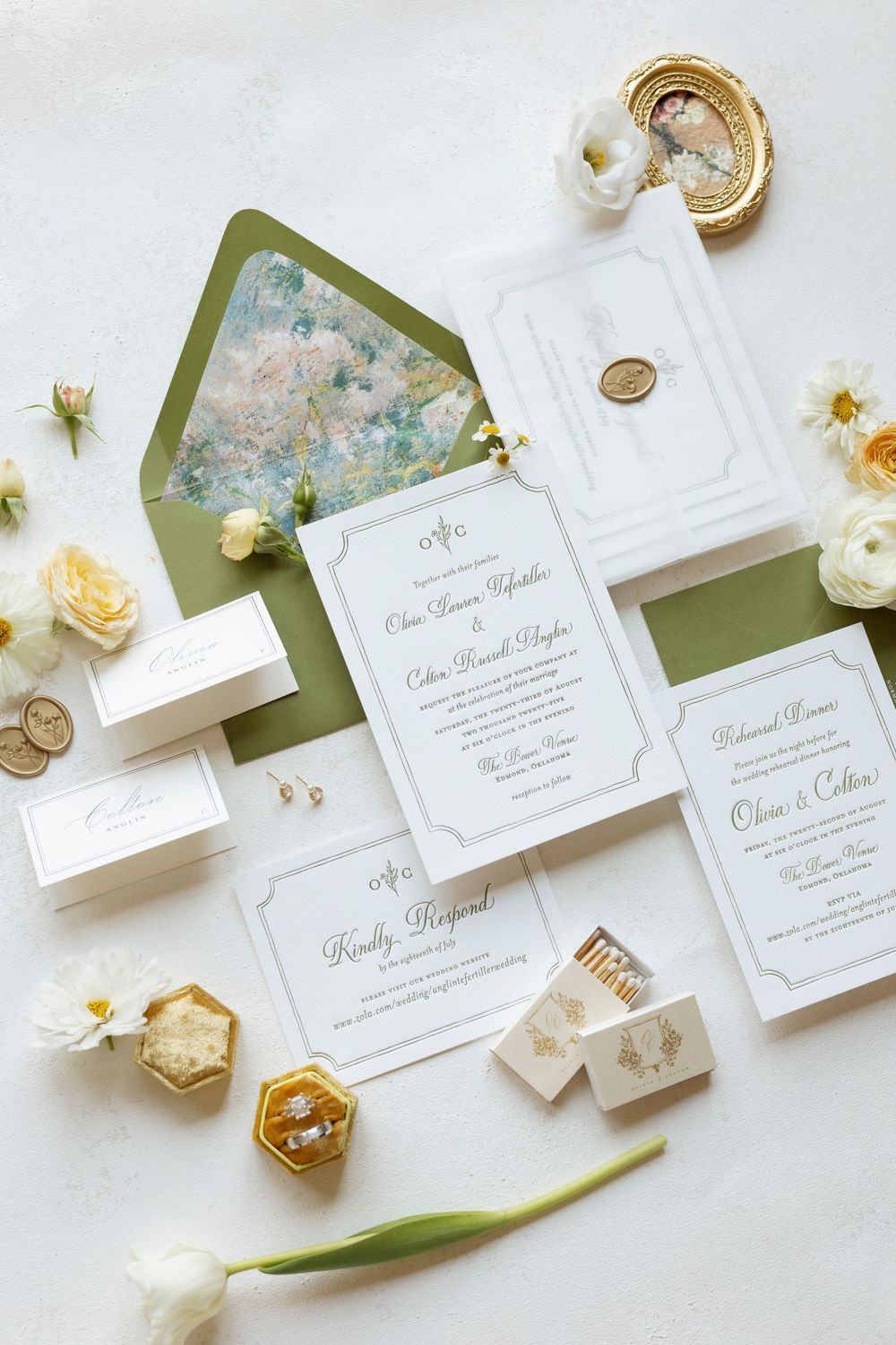 Elegant white wedding invitation suite with green envelopes and delicate floral accents displayed on marble.