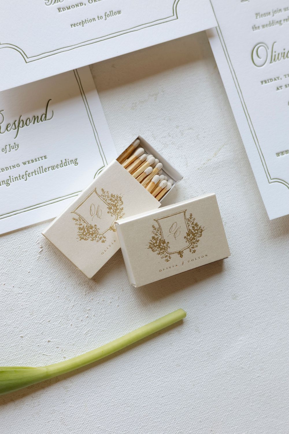 Close-up of white wedding stationery with gold foil details and green accents.