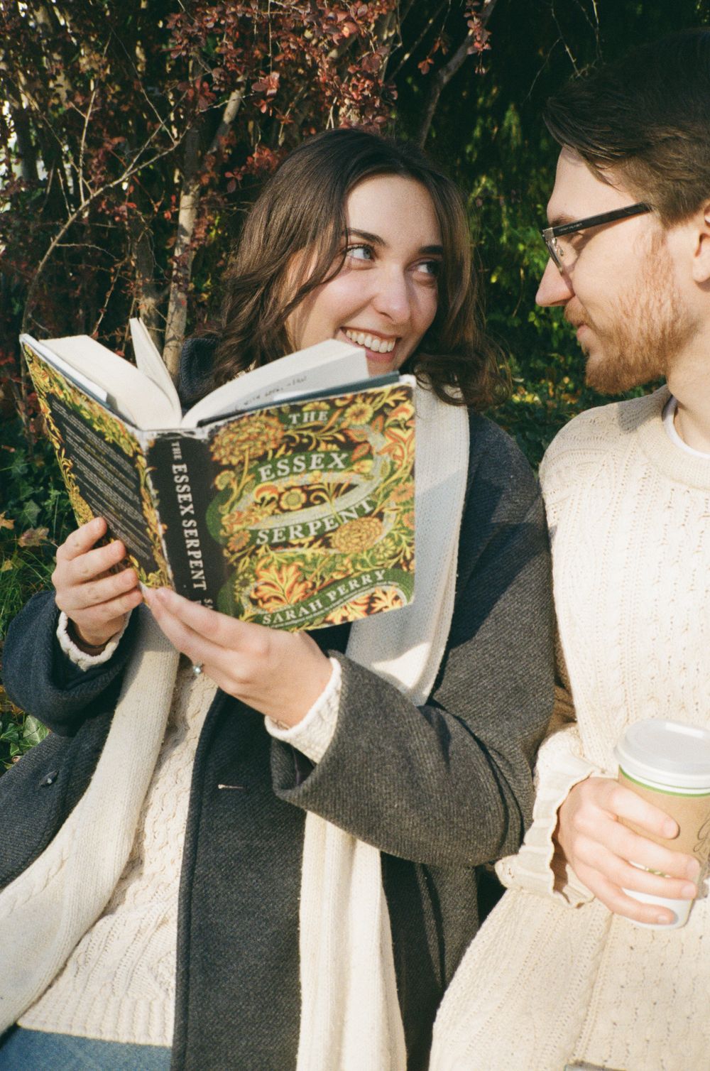 A couple shares a playful moment outdoors while reading a book together in autumn.