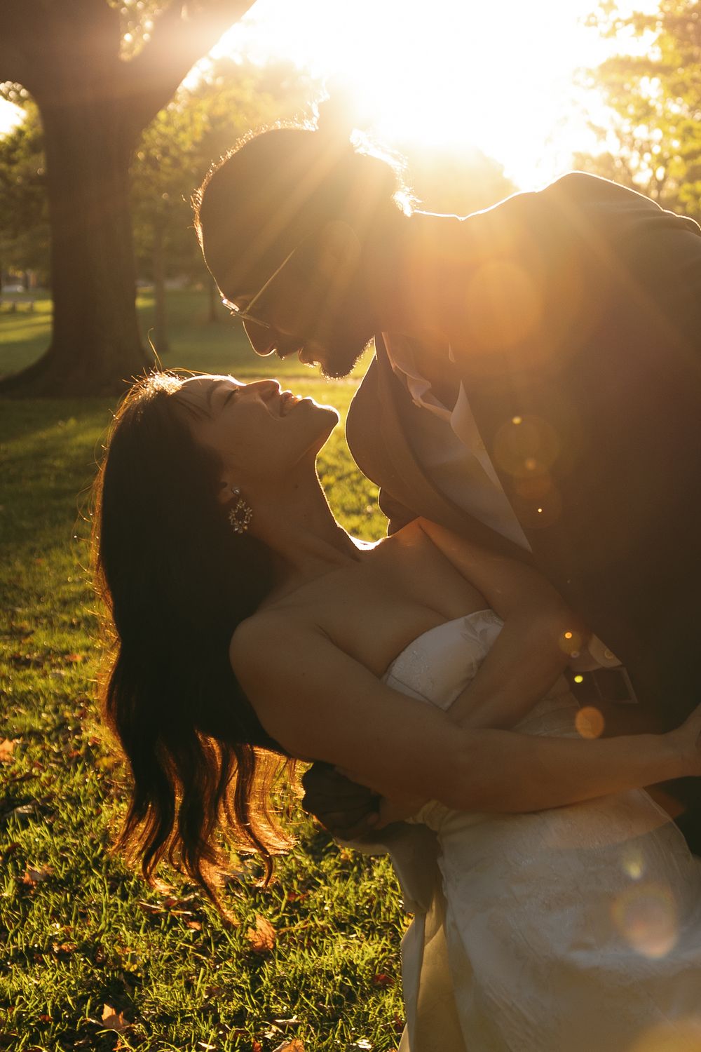 A couple embraces in a romantic golden sunset on grassy lawn while sunlight creates a dreamy backlit glow.