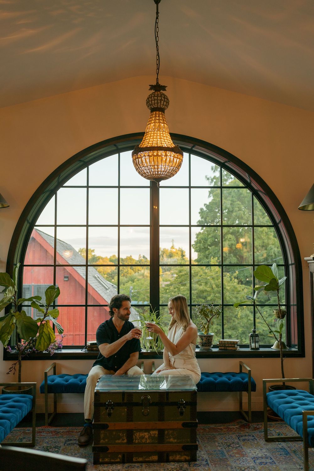Couple enjoying drinks together in a rustic restaurant with arched windows and chandelier lighting.