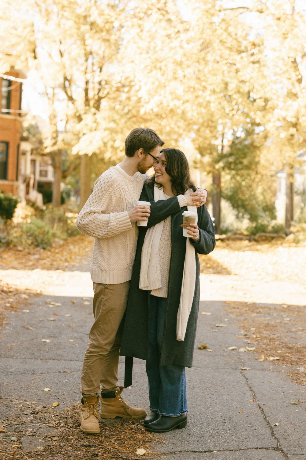 A couple shares a tender moment outdoors on a fall day with golden leaves in the background.
