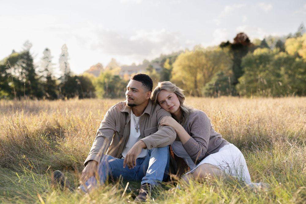 A couple shares tender moments together while relaxing in a sunlit meadow during golden hour.