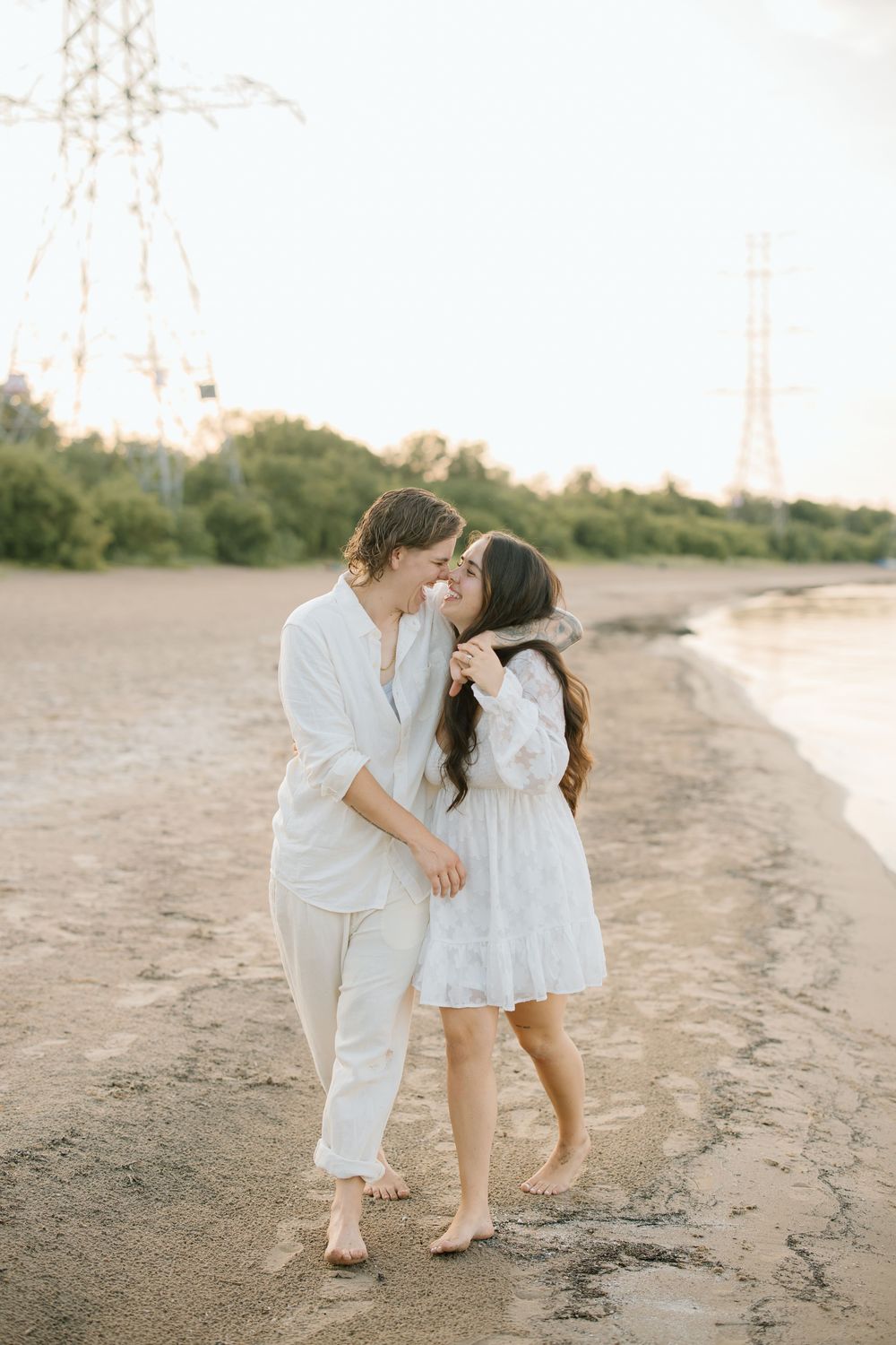 Two young children in white outfits share a sweet moment together on a sandy beach at sunset.
