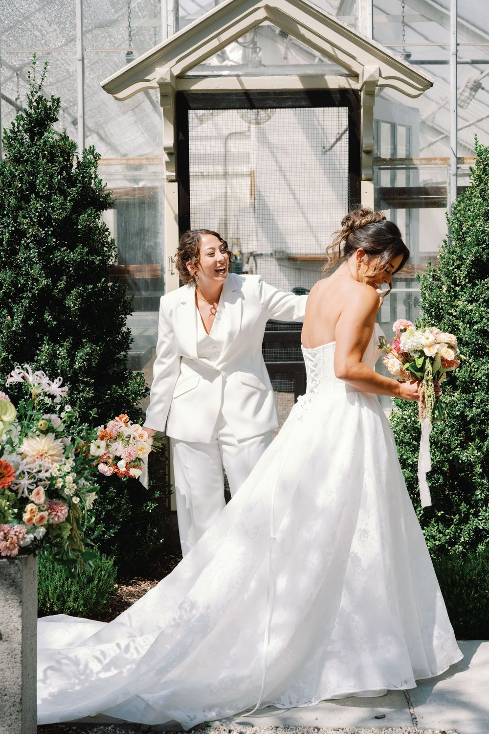 A joyful couple in wedding attire share a romantic moment in a sunlit garden setting with floral arrangements.