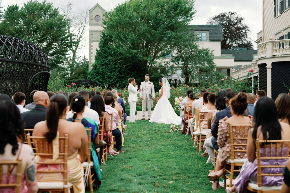 A group of wedding guests gather on a green lawn outside during a summer outdoor ceremony.