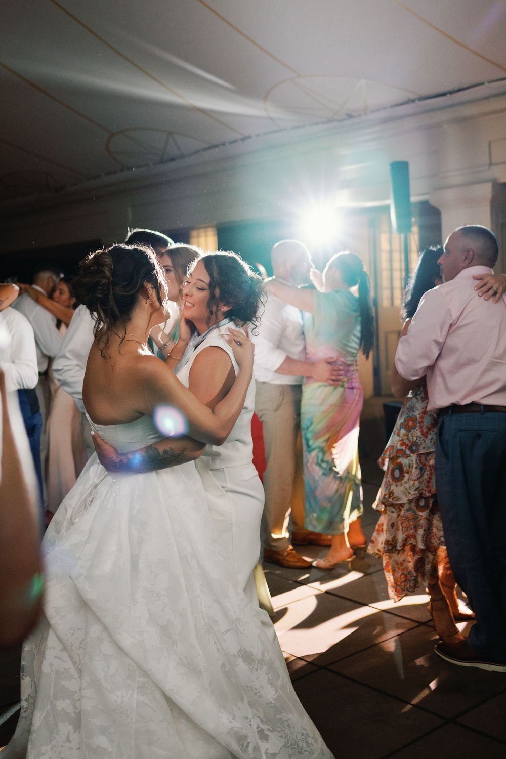 Couples dance together during a romantic wedding reception with dramatic lighting and lens flare effects.