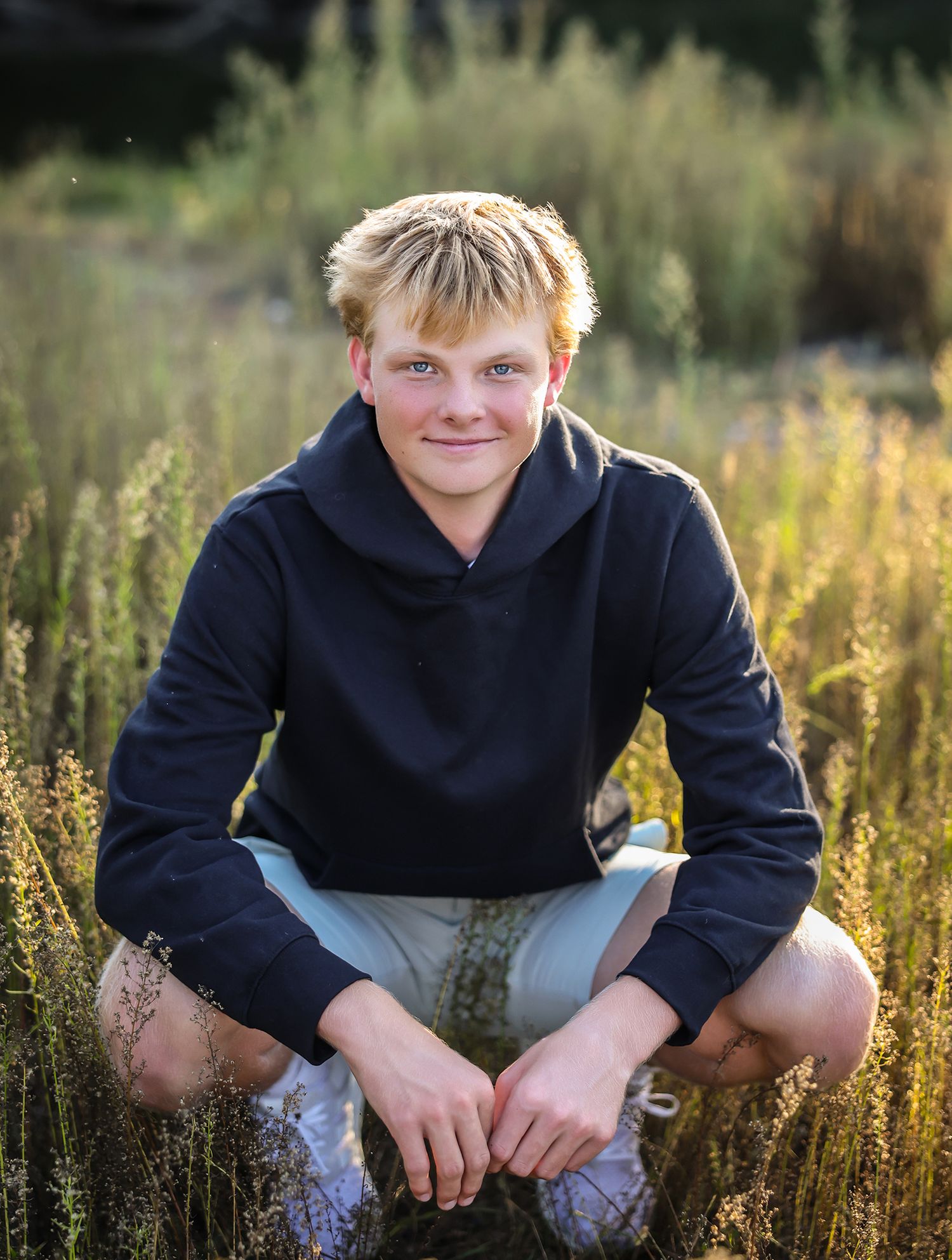 Outdoor portrait in tall grass wearing navy hoodie during golden hour.