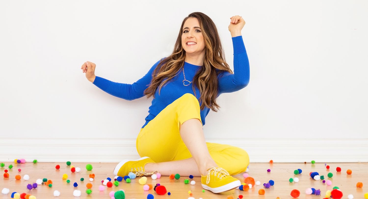 Woman in bright yellow dress and blue cardigan dances joyfully among colorful confetti on white background.