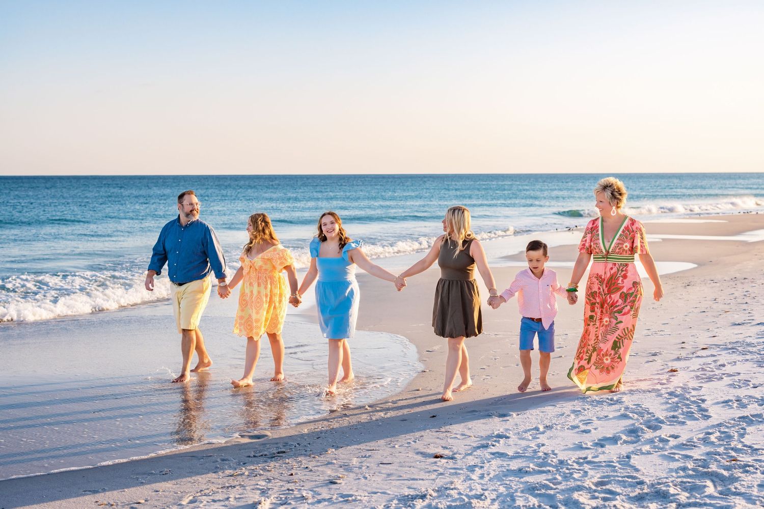 Group walking together along a sandy beach shoreline at sunset with ocean waves in the background.