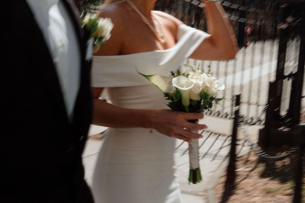 Close-up of a white bridal bouquet being held against an elegant white wedding dress.