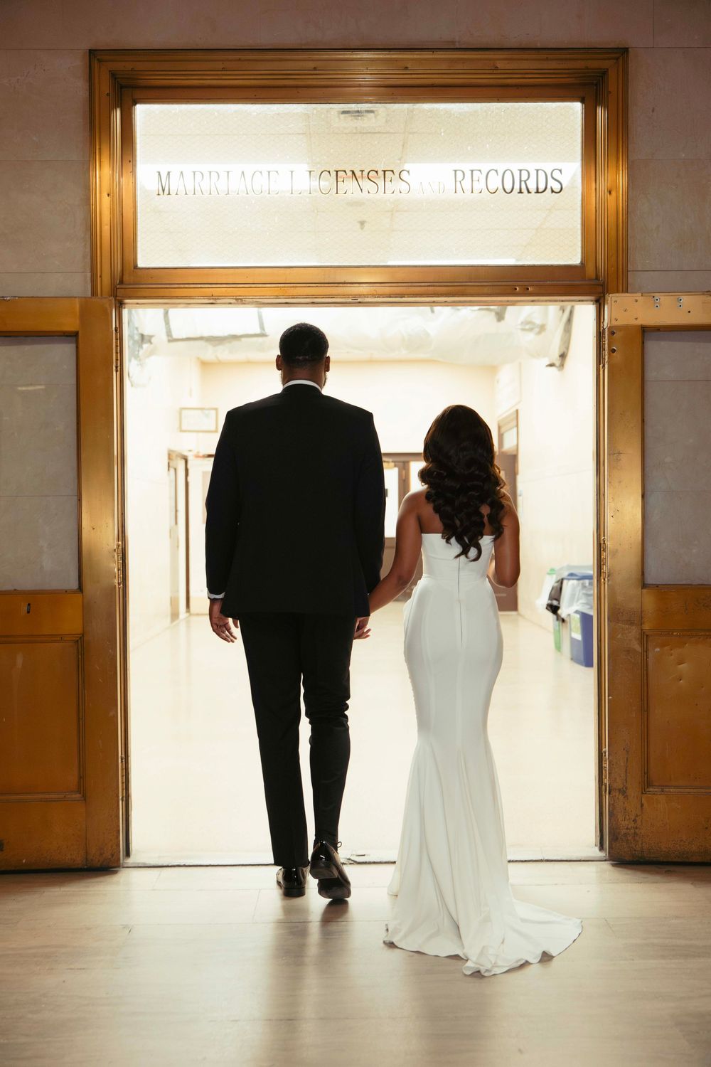 Couple walking towards illuminated doorway in empty hallway.