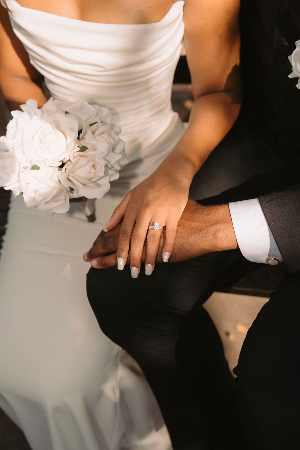 Close-up detail of wedding rings and white bouquet with bride in white dress and groom in black suit.