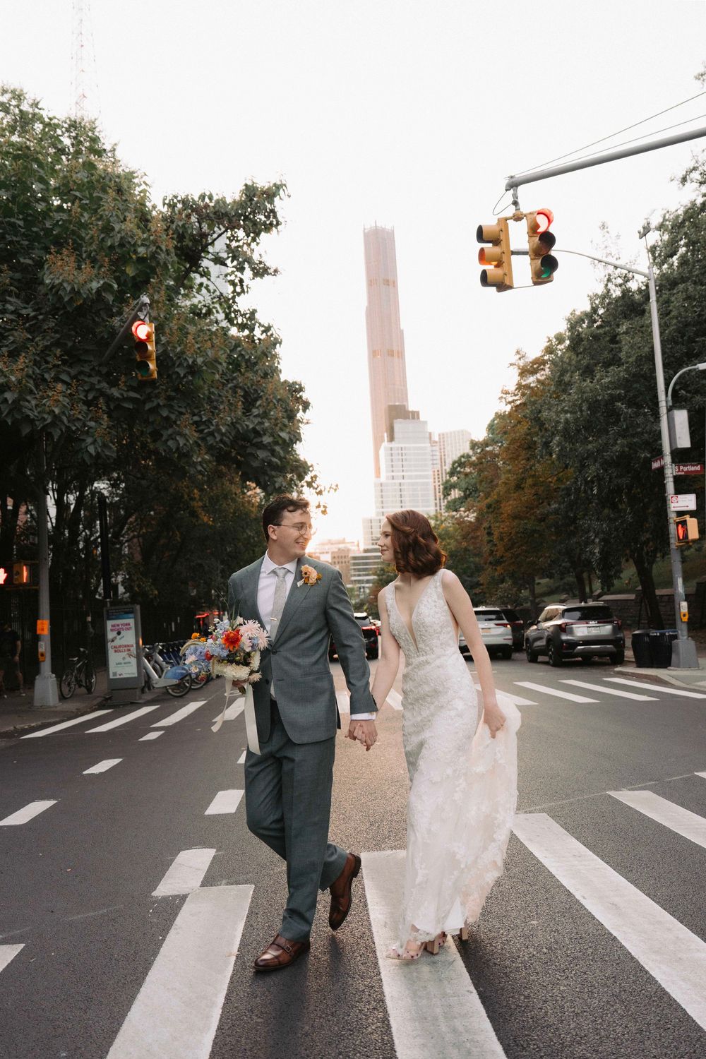 A couple recreates the iconic Beatles Abbey Road crossing pose on a city street with skyscrapers in the background.