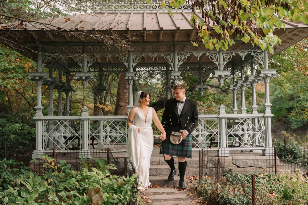 A wedding couple poses for romantic photos in a lush garden setting with decorative architecture.
