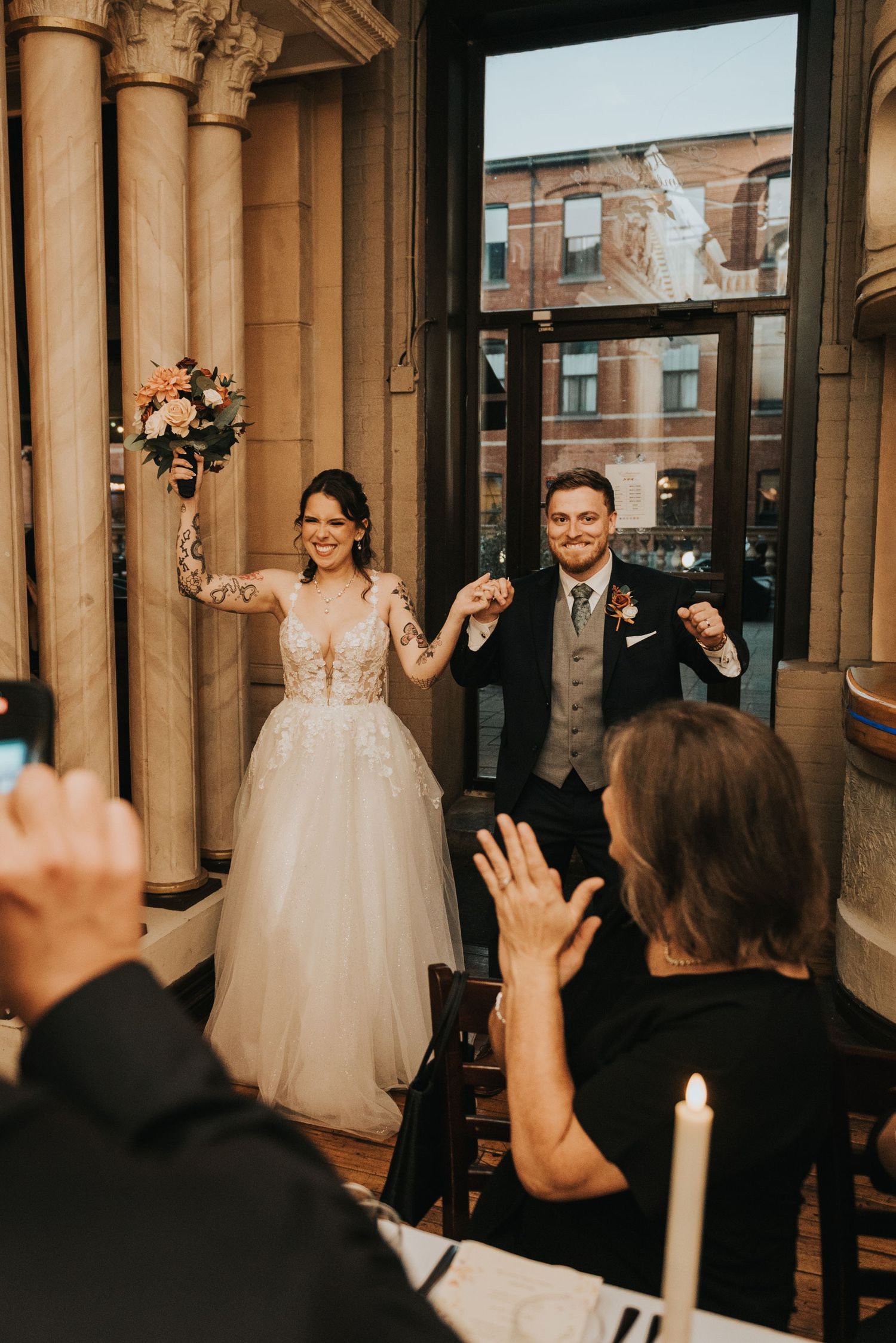 Newlywed couple celebrates with guests in elegant venue with classical columns during wedding reception.