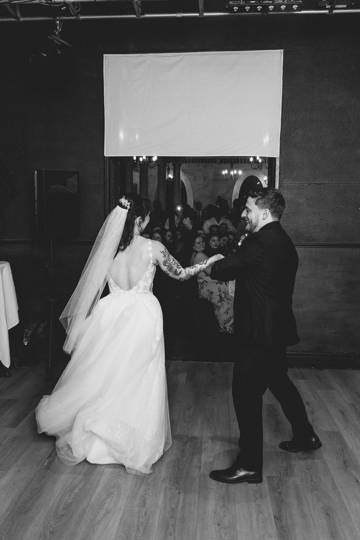A bride and groom perform a romantic dance sequence on a wooden ballroom floor during their wedding reception.