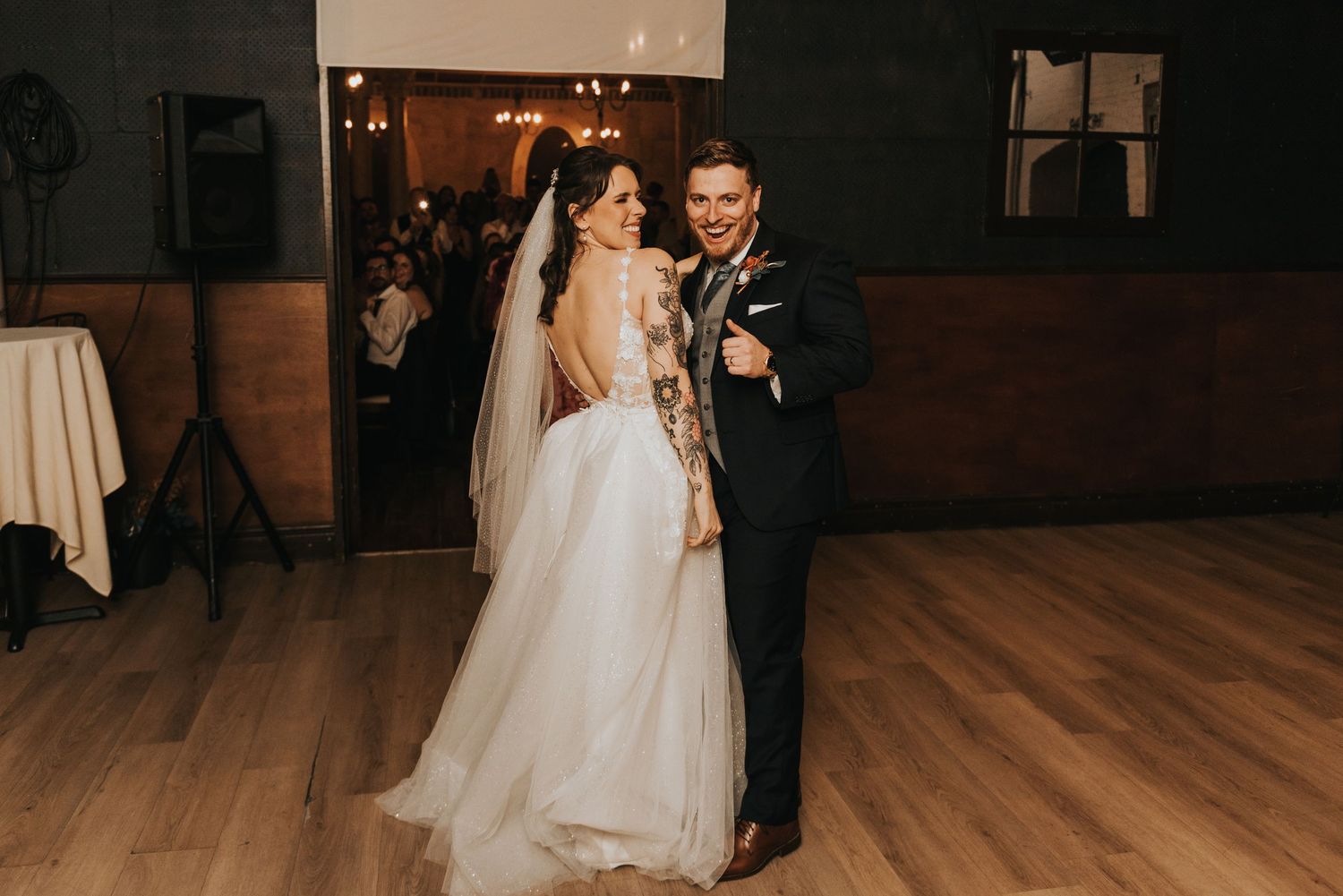 A couple dances together on a wooden floor during a wedding reception in a dimly lit venue.