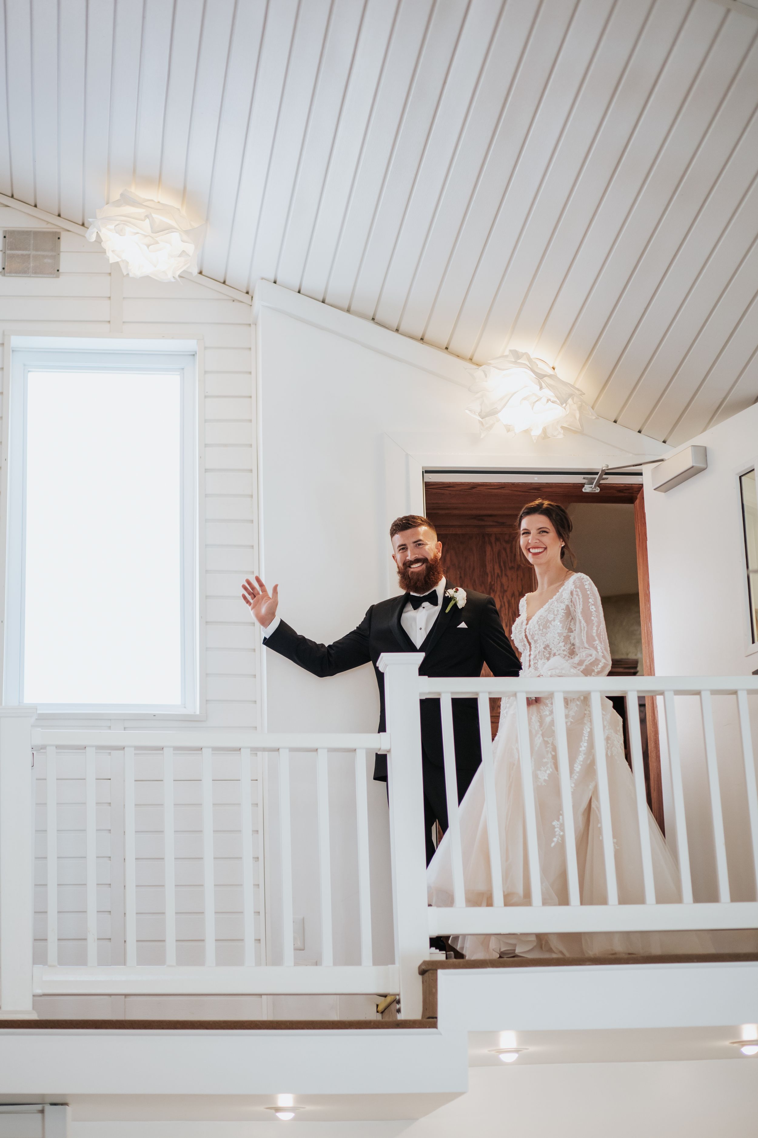 A joyful moment captured in a bright white chapel balcony during a wedding celebration.