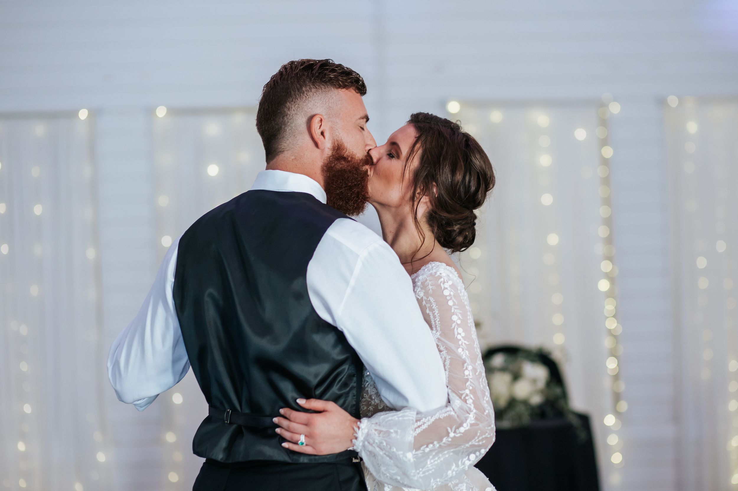 Romantic first dance between newlyweds in a reception hall decorated with twinkling string lights.