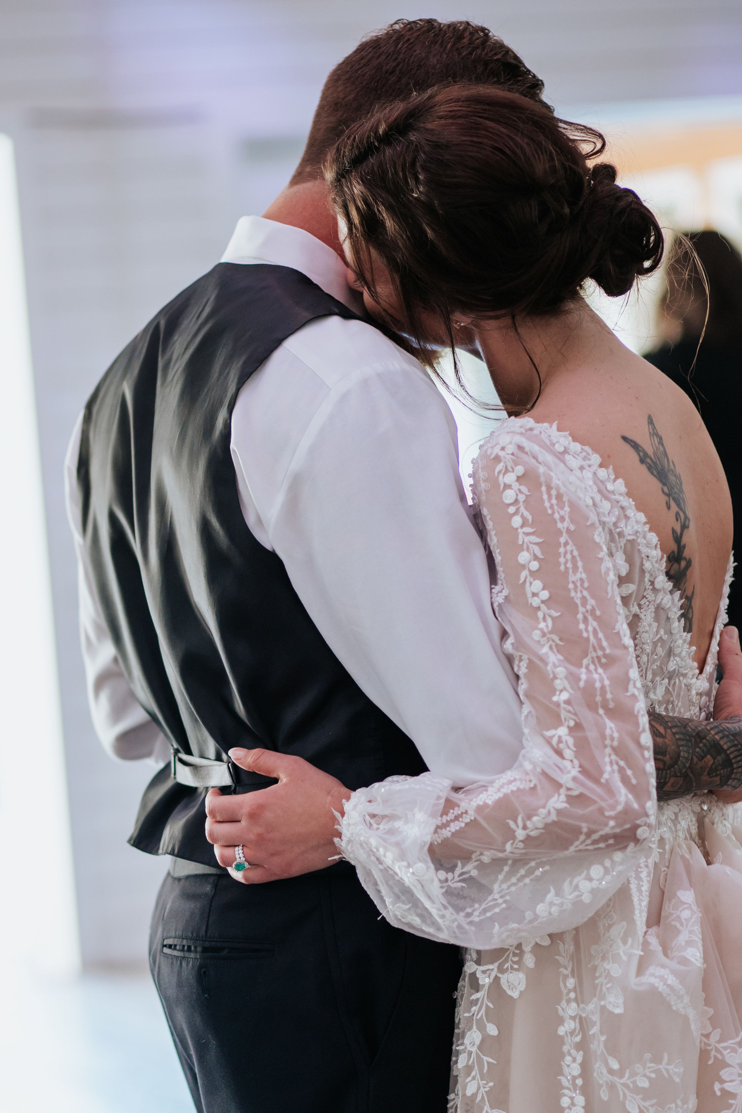 Tender moment during wedding dance with bride in delicate lace dress and groom in black vest.