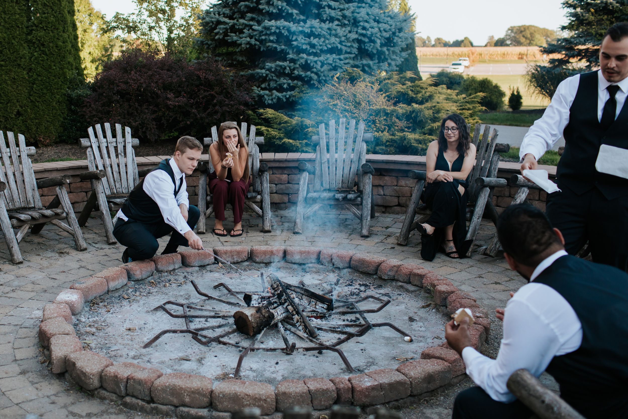 Wedding guests gathered around stone fire pit during outdoor reception.
