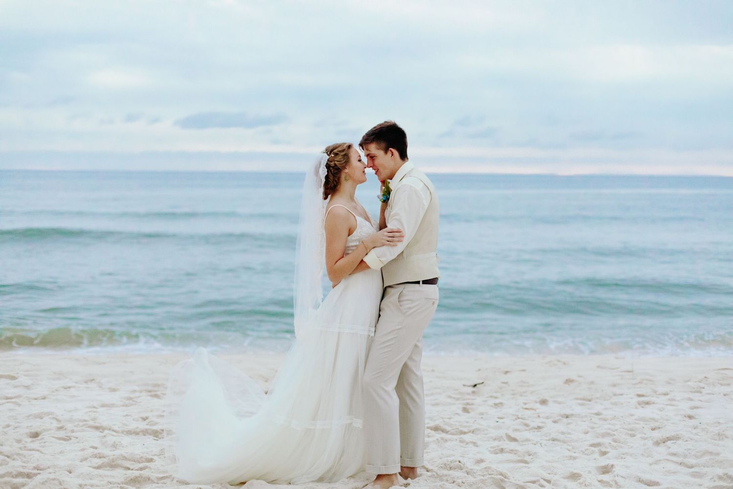 Romantic bride and groom sharing an intimate moment on a sandy beach with ocean waves in the background.