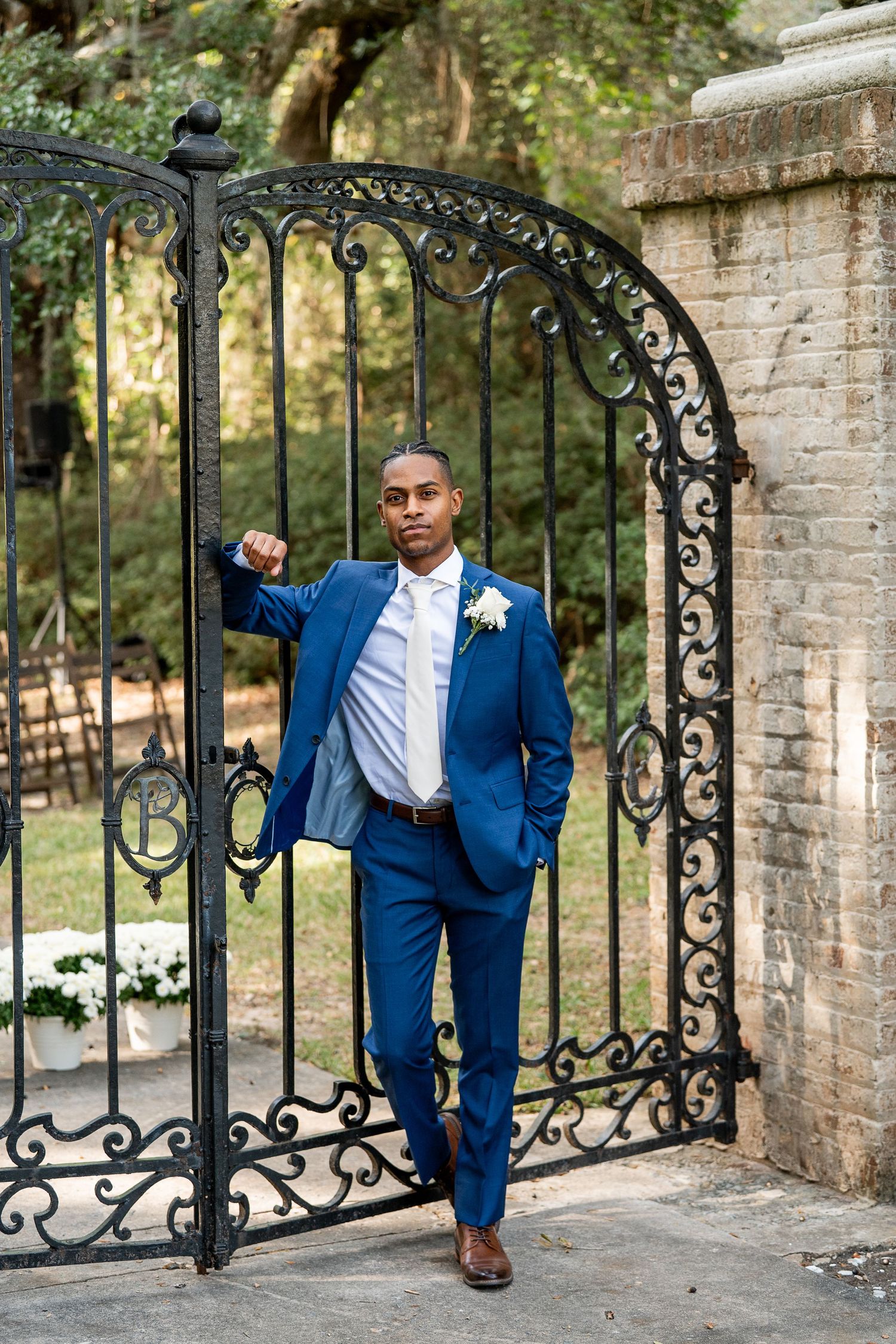 Groom in navy suit poses confidently against ornate wrought iron gates.