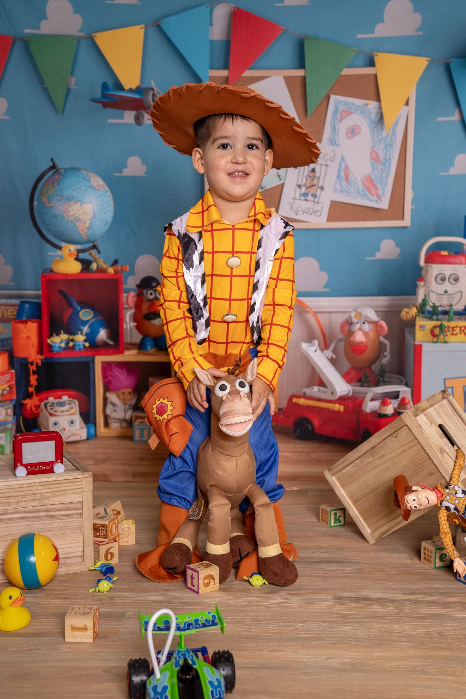 Boy dressed as Woody from Toy Story riding a Bullseye horse toy in a colorful playroom with toys and decorations.