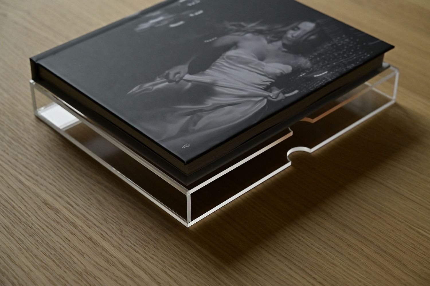 Black and white wedding photo book displayed in clear acrylic holder on wooden surface.
