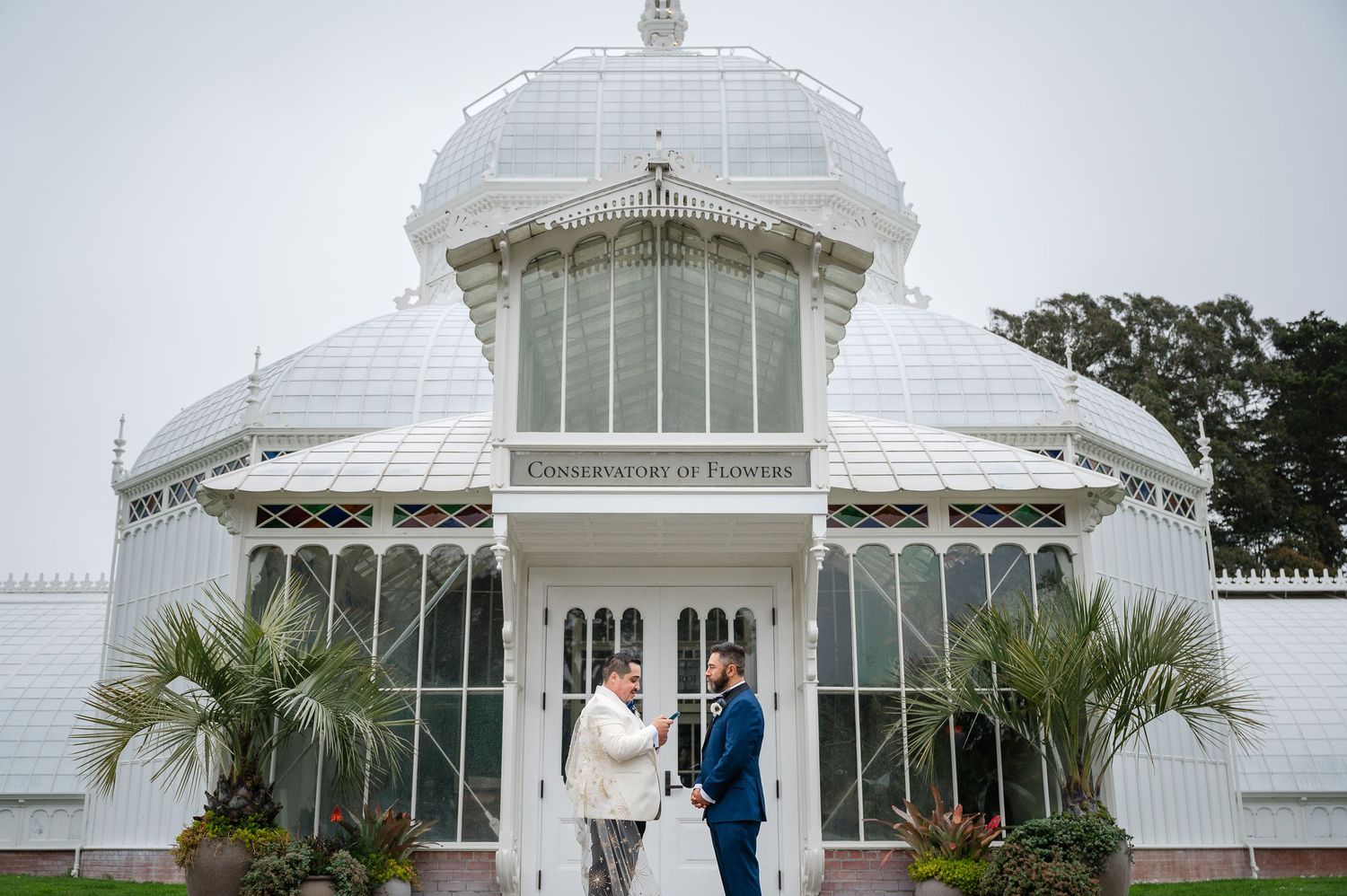Couple exchanging vows in front of the Conservatory of Flowers in San Francisco on a misty wedding day.