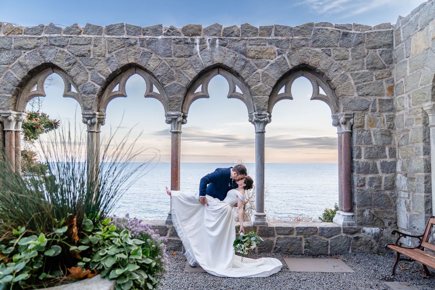 Bride and groom dip kiss outside Hammond Castle in Gloucester at sunset.