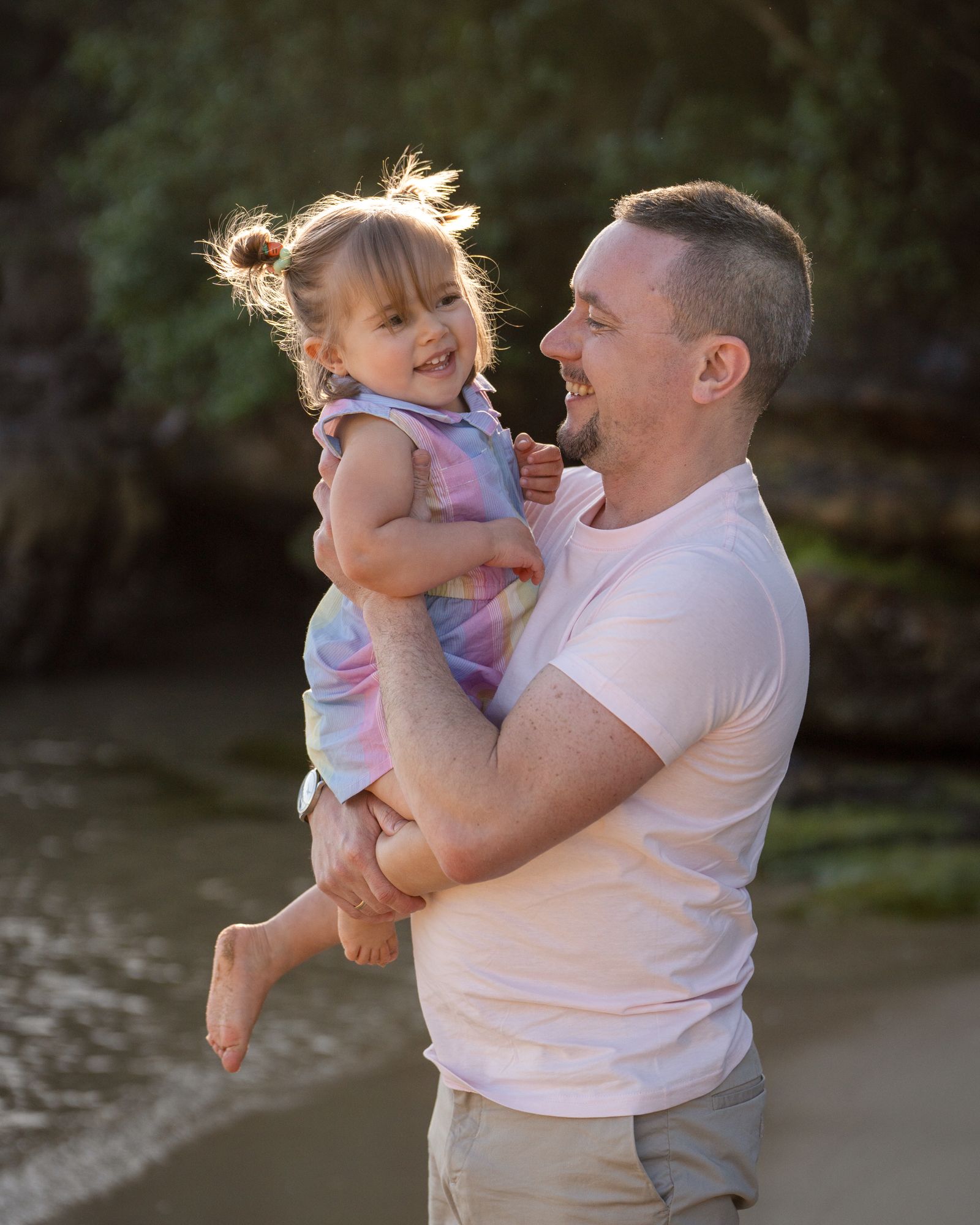 A tender moment shared between parent and child playing together on a sandy beach near the water during father's day photoshoot in sydney