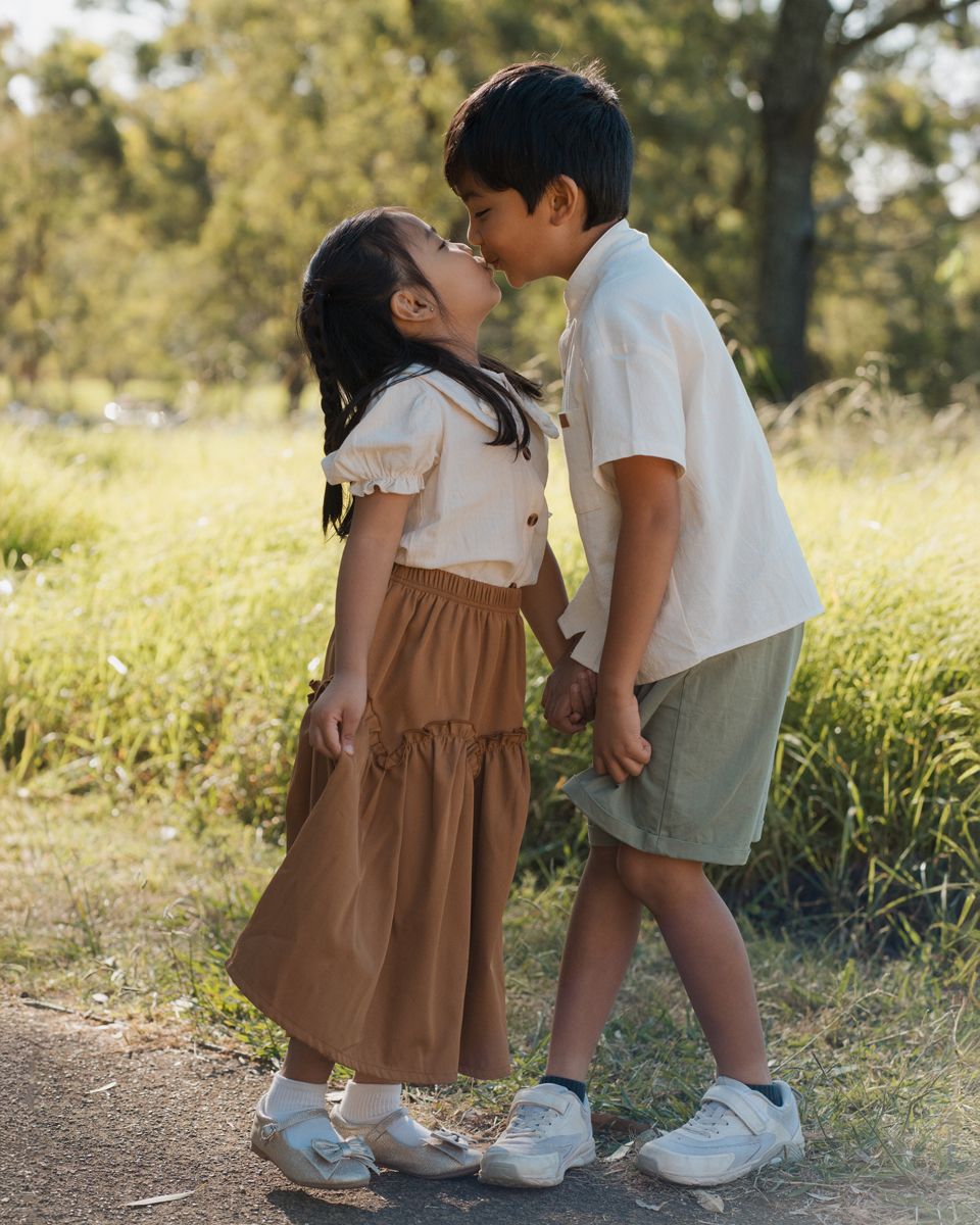Young children sharing a sweet nose-to-nose moment outdoors, holding hands in matching neutral outfits during family photoshoot rouse hill