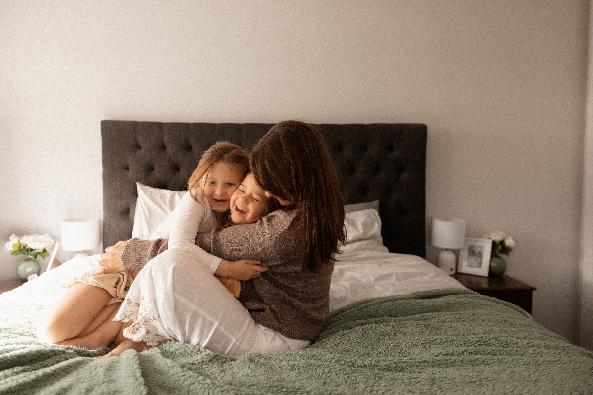 mum holding and cuddling her daughters on the bed at home