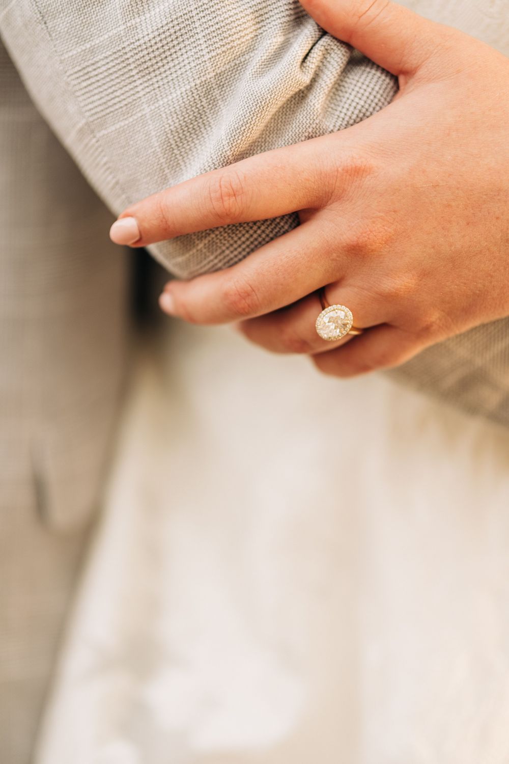 Close-up of oval diamond engagement ring on gold band worn on woman's hand at engagement party.