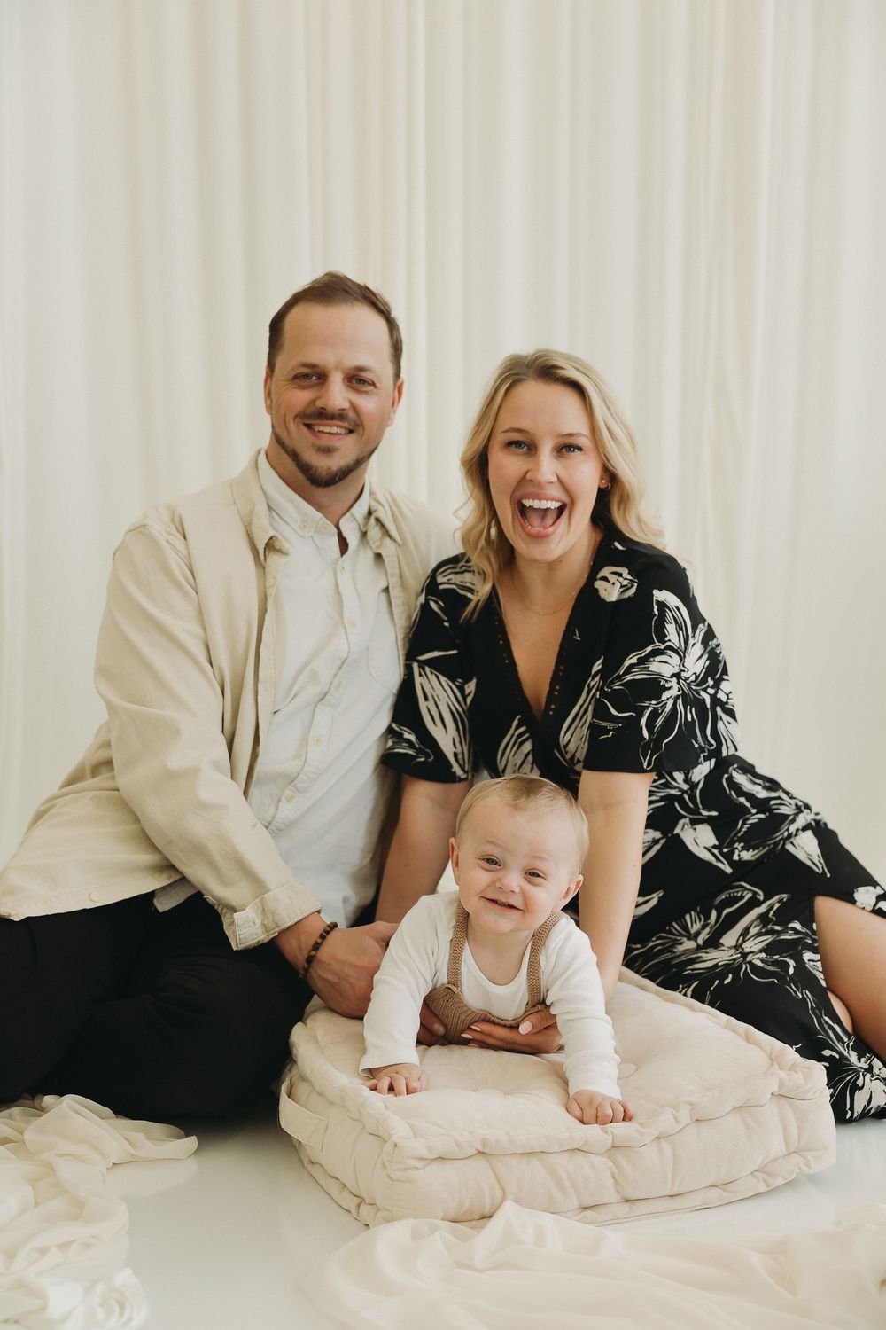 Happy family portrait with parents and baby on white background, smiling couple with infant in white onesie.