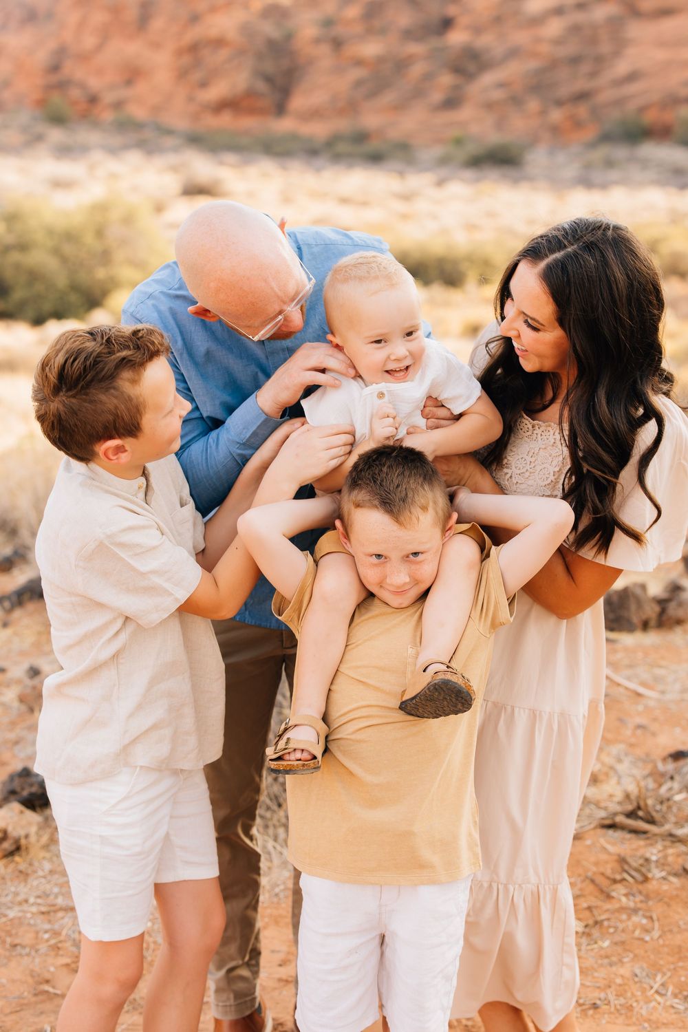Playful family of five laughing together against red rock desert landscape on a sunny day.