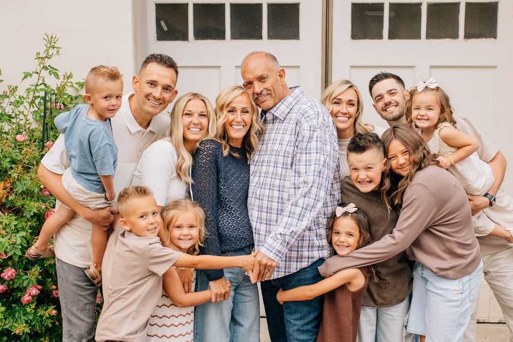 Large extended family of adults and children smiling together outdoors in front of a white garage door.
