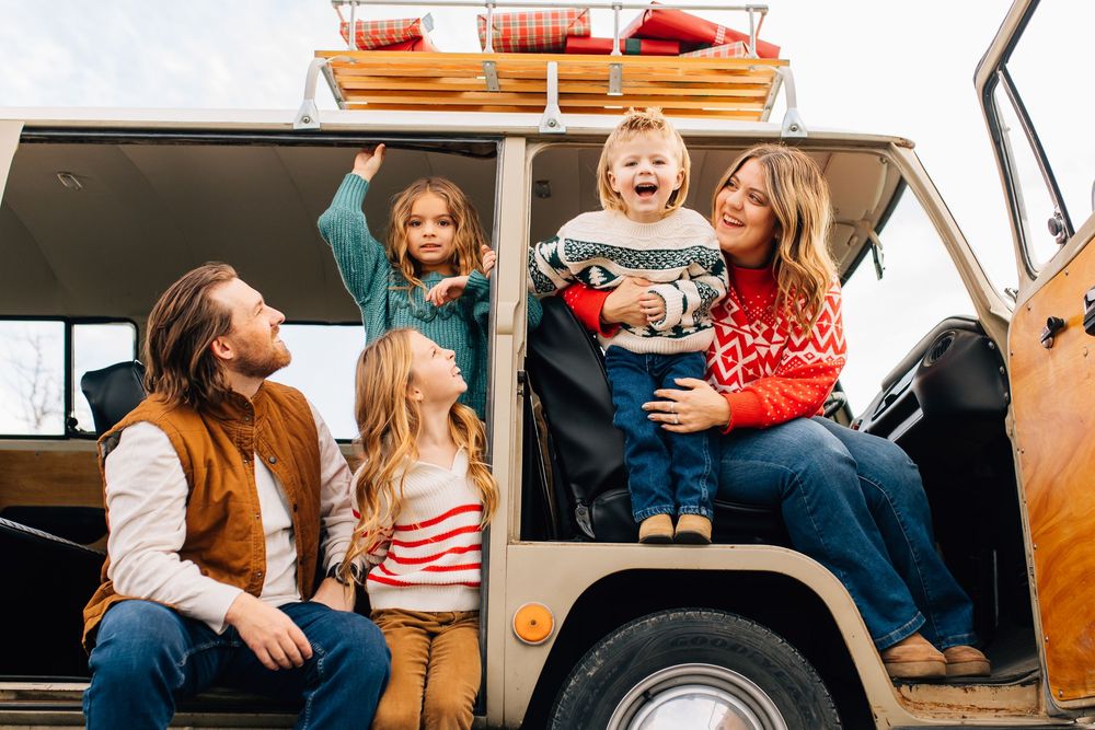 Joyful family with three kids laughing together at the back of a vintage camper van outdoors.