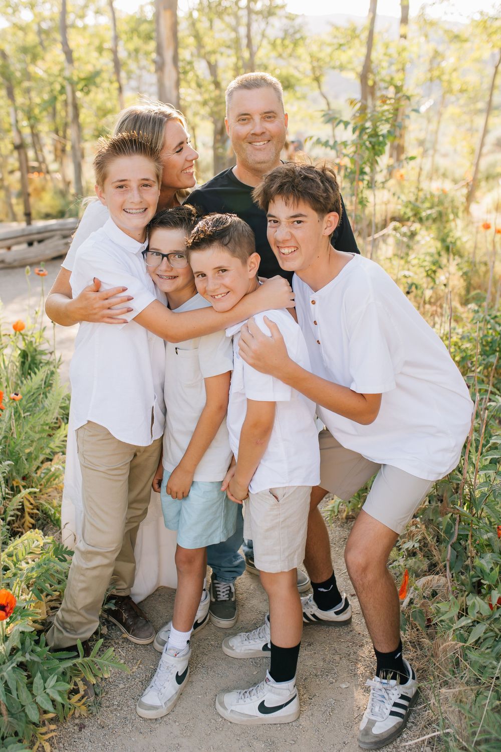 Family portrait of parents with four boys in white shirts posing outdoors among wildflowers.