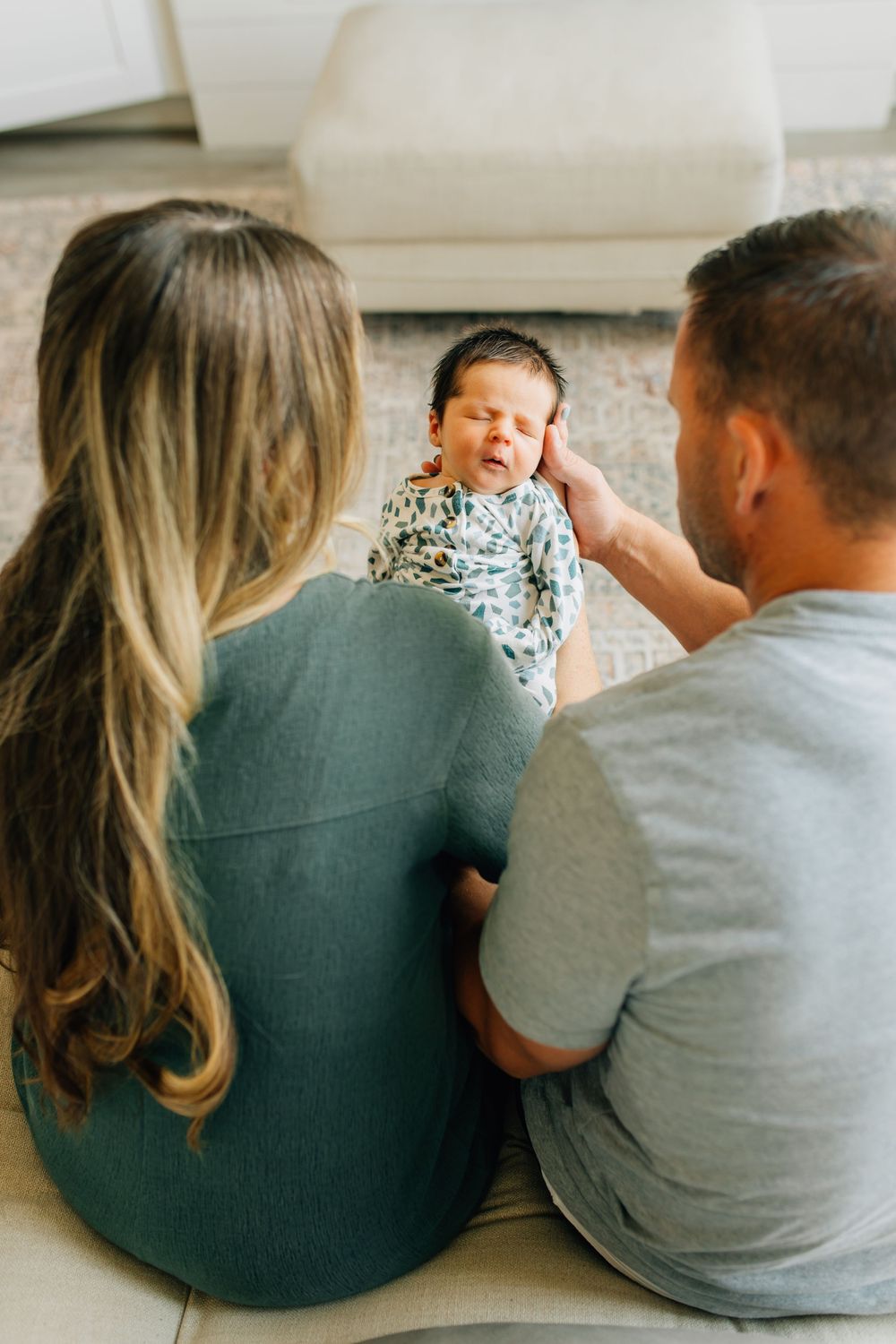 New parents sitting on the floor gazing lovingly at their newborn baby lying on a soft rug.