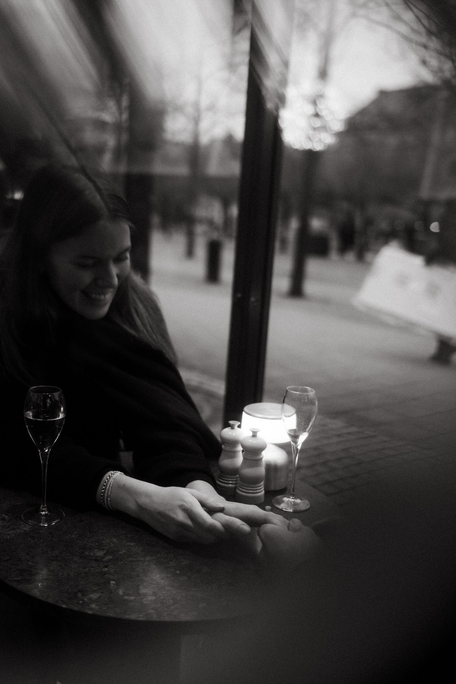 woman holding her fiancée's hand sitting in a restaurant, smiling while being captured by surprise proposal photographer in Stockholm