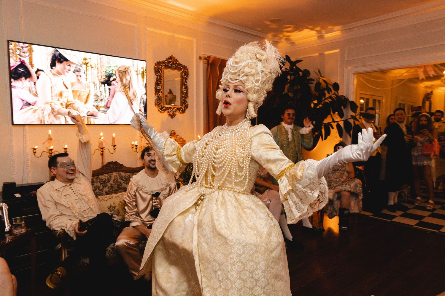Performer in ornate gold Marie Antoinette costume dancing at elegant themed party with guests watching in background.
