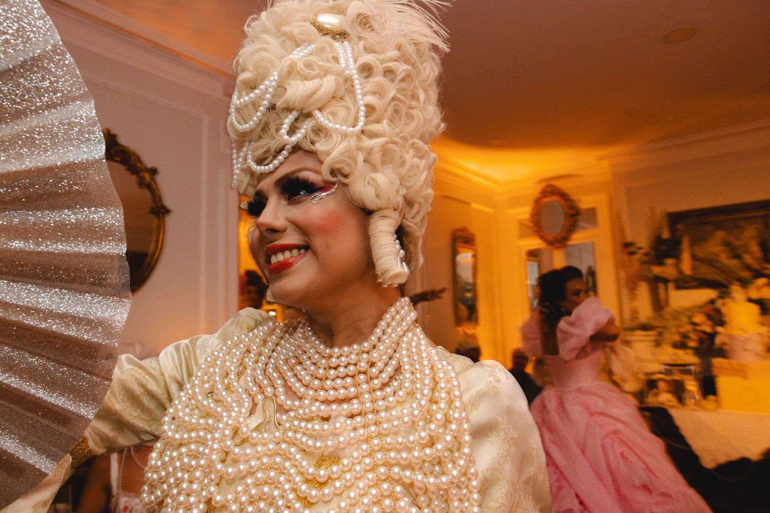 Performer in elaborate Marie Antoinette costume with pearl necklaces and tall white wig at elegant party.
